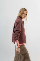 Chaqueta corta tipo blazer color marrón, confeccionada en tela de lana afieltrada. Tiene cuello camisero, silueta cuadrada, cierre frontal con botones y bolsillos delanteros.