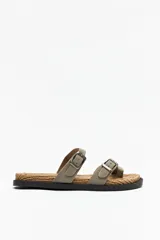 Sandalia plana con base de fibra trenzada y dos tiras ajustables con hebillas metálicas. Presenta un diseño con suela de goma negra y tiras en color verde oliva.