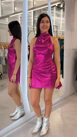 Vestido corto fucsia de tejido metalizado con brillo, diseño sin mangas, cuello alto y falda cruzada.