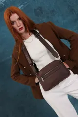 Bandolera de diseño moderno y funcional, confeccionada en nylon color marrón claro. Cuenta con múltiples compartimentos con cierre metálico, herrajes plateados y una correa ancha ajustable con detalle de marca.