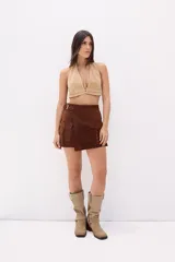 Minifalda beige de cuero con diseño cruzado, cinturón con hebilla metálica y bolsillo tipo cargo con solapa.
