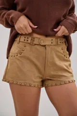 Short de gamuza color beige con detalle de tachas metálicas en los bolsillos y en el ruedo. Cuenta con un cinturón integrado con hebillas y ojales metálicos.