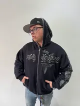 Campera reversible con cierre frontal, diseño oversize. Un lado es de algodón negro con estampados y bordados gráficos, mientras que el otro lado es de tela polar gris de pelo largo. Cuenta con capucha, puños y ruedo acanalados.
