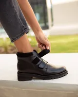 Bota corta de cuero color negro, estilo botín, con suela track gruesa y dos tiras ajustables con hebillas brillantes en el empeine.