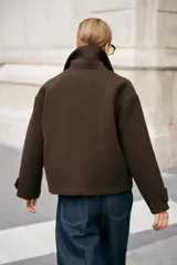 Abrigo corto de paño en color marrón chocolate, con cuello de solapa, cierre frontal cruzado con botones y mangas largas con detalle de trabilla y botón en los puños.