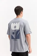 Remera oversize gris de algodón, de manga corta, con estampa en la espalda de formas botánicas abstractas y el logo de la marca.