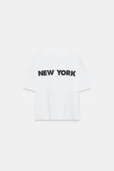 Remera oversize blanca de algodón con cuello redondo, manga corta y estampa con la inscripción 'NEW YORK' en color negro en el frente.
