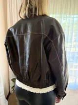 Campera de eco cuero en tono marrón con efecto desgastado, corte oversize y cierre frontal. Presenta costuras marcadas, bolsillos frontales y puños con botones.