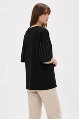Remera negra de algodón con cuello redondo, mangas cortas y diseño holgado, decorada con líneas verticales de strass.