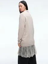 Sweater de tejido de punto color beige, con cuello redondo y mangas largas. Presenta un diseño de largo extendido con un delicado aplique de encaje en el ruedo inferior.
