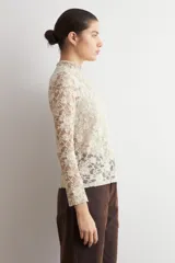 Media polera de encaje color beige, con cuello alto y mangas largas, de diseño translúcido y ajustado al cuerpo.