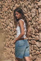 Bermuda de tiro medio confeccionada en denim de color negro gastado, con diseño de cinco bolsillos, trabillas para cinturón y cierre frontal con cremallera y botón metálico.