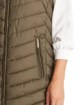 Chaleco puffer capitoneado color verde militar, con cierre central, bolsillos delanteros con cierre, jareta de ajuste en la espalda y capucha no desmontable. Tiene forro interno.