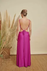 Vestido largo de satén color fucsia, con escote en V, aberturas laterales en la cintura y detalle de aro metálico en el centro del pecho. Posee breteles finos y falda con caída fluida.