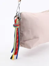 Bandolera rosada con cierre superior y correa ajustable. Cuenta con un detalle colgante de cordones coloridos en el lateral.