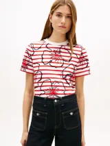 Remera Tommy Hilfiger de corte regular confeccionada en puro algodón con punto interlock. Presenta un diseño de rayas horizontales rojas y blancas con estampado floral gráfico superpuesto, cuello redondo y mangas cortas.