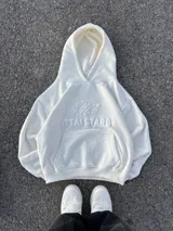 Hoodie de color blanco off-white con diseño de capucha, bolsillo frontal tipo canguro y bordado en relieve con el texto ITTAI STARS y un logo caligráfico.