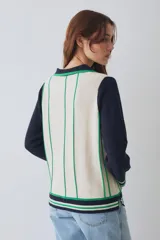 Remera tejida de punto estilo polo con mangas largas en color crema y cuerpo en color bordó con rayas verticales amarillas. Presenta cuello tipo polo, aberturas laterales y un pequeño parche circular con diseño de sol en el pecho.