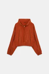 Chaqueta color naranja óxido de tejido fluido, con cuello subido, manga larga acabada en elástico, bolsillos laterales de vivo, bajo elástico y cierre frontal con cremallera.