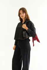 Camisa de corte oversize y estilo casual, confeccionada en algodón negro con costuras a contratono en color blanco. Presenta cuello camisero, cierre frontal parcial, mangas largas y un bordado distintivo en el puño.