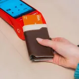 Billetera tarjetero automática con estructura de aluminio y revestimiento de cuero bicolor en tonos verde oliva y beige. Cuenta con un cierre de broche a presión y el logo de la marca grabado en la parte inferior.