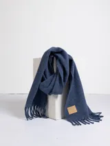 Bufanda de tejido suave en color rosado, con diseño liso y terminaciones con flecos en los extremos. Incluye una etiqueta de cuero sintético con el logo de la marca en uno de los bordes.
