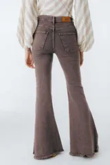 Pantalón de jean azul oscuro, corte acampanado (flare) de tiro alto, con costuras visibles en contraste y bordados tonales en la parte inferior de las piernas. El ruedo es deshilachado.