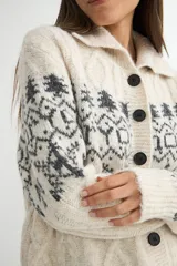 Saco de punto con cuello tipo polo, cierre frontal de botones oscuros y diseño de estampado jacquard en tonos grises y beige. Presenta mangas largas con puños acanalados y textura suave.