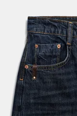Jeans de tiro medio, color azul oscuro lavado, con corte balloon fit (holgado en muslos y estrechado en el tobillo). Presenta cinco bolsillos, cierre frontal con botones y detalle de trabilla con hebilla en la parte trasera de la cintura.