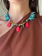 Collar corto de diseño artesanal con cuentas de cristal checo, piedras facetadas y colgantes en forma de colmillos de nácar teñidos en color turquesa y gotas de resina en color rojo. Incluye cadena de acero quirúrgico para regular el largo.