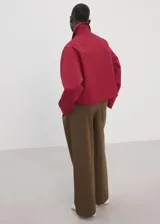 Chaqueta corta de algodón en color rojo, con cuello camisero, manga larga y cierre frontal de botones oscuros. Presenta dos bolsillos con solapa en el frente.