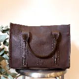 Cartera de cuero color tostado, estructurada, con doble asa de mano, correa desmontable y dos bolsillos frontales verticales con cierre. Presenta detalles de costuras pespunteadas y el logo de la marca grabado en la parte inferior.