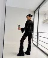 Conjunto de dos piezas compuesto por top de manga larga con cierre frontal de lazos y pantalón de corte acampanado. Ambas prendas están confeccionadas en encaje negro con diseño de franjas horizontales superpuestas.