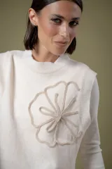 Chaleco de lana color crema con diseño de flor bordada en relieve en el frente, cuello redondo y aberturas laterales en el ruedo.