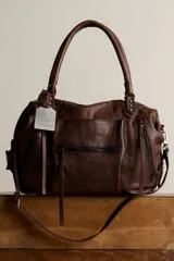 Bolso tote de cuero lavado, color marrón, con amplio compartimento principal, bolsillos exteriores con cremallera, asas de mano y correa desmontable y regulable.