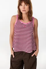 Musculosa de corte holgado con diseño a rayas horizontales en tonos marrón y crudo. Presenta ribetes en color fucsia en el cuello redondo y en las sisas, además de un pequeño bordado decorativo en el centro del pecho.