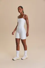 Jumpsuit corto de diseño ajustado con escote cuadrado y breteles finos. Confeccionado en tejido técnico con acabado ligeramente brillante y textura acanalada, ofrece compresión media y alta elasticidad.