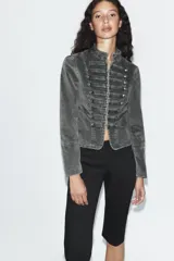 Chaqueta entallada de terciopelo color gris con efecto acid wash, cuello subido, manga larga y cierre frontal con ganchos metálicos. Presenta detalles de pasamanería con falsos botones en el delantero de inspiración militar.
