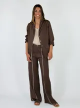 Pantalón marrón de lino de corte recto y holgado, con costuras decorativas claras a lo largo de las piernas.
