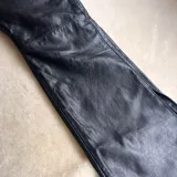 Pantalón de cuero vacuno negro, de corte recto y tiro medio. Presenta costuras horizontales a la altura de la rodilla y aberturas laterales en el ruedo. Incluye un botón de guampa irregular como detalle distintivo en la cintura.