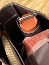 Bolso tipo tote de neopreno en color verde oliva, con correas de hombro en color rojo y detalles en blanco. Cuenta con broches imantados laterales para ajustar su forma y un bolsillo interno de red.