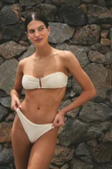 Conjunto de bikini color hueso, confeccionado en lycra texturada. El corpiño es strapless con tiras ajustables y hebilla metálica en el centro. La bombacha es vedetina y está forrada.