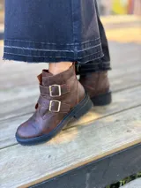 Botas cortas de cuero color marrón con suela track negra. Presentan dos correas ajustables con hebillas metálicas plateadas en el empeine y cierre lateral interno.