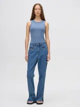 Pantalón de denim color marrón, de tiro alto y calce ochentoso con terminación estilo oxford. Cuenta con apliques metálicos decorativos alrededor de los bolsillos y a lo largo de las costuras exteriores.
