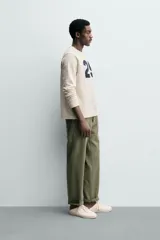 Camiseta relaxed fit de algodón con estructura waffle, color beige. Presenta un parche con el número "29" en azul marino en el pecho. Tiene cuello redondo y manga larga con acabados en rib.