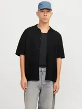 Polo de tejido estructurado negro, con hombros caídos, ajuste holgado, cuello tipo polo, mangas cortas y cierre frontal con botones.