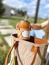 Bolso tote de cuero color taupe con textura croco y detalles en verde. Tiene doble asa de mano de cuero marrón y un dije de cuero con flecos. No tiene división interna.