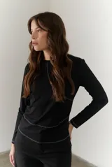 Remera blanca de manga larga con cuello redondo y costuras decorativas en contraste de color negro.