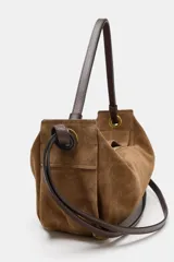 Bolso de mano formato alargado confeccionado en piel, con doble asa, una de mano y otra de hombro, con detalle de nudos y ojales metálicos. Cuenta con cierre mediante solapa y cremallera, y bolsillo interior con cremallera.