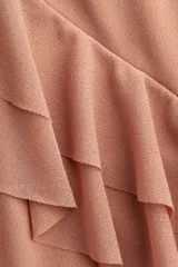 Vestido largo sin mangas de punto liviano, color rosado, con escote de pico pronunciado y ribetes de volado. Presenta volados de doble capa bajo el busto que se extienden por la cintura trasera. El vestido es forrado.